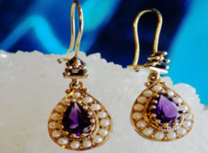 A pair of earrings with purple stones and pearls.