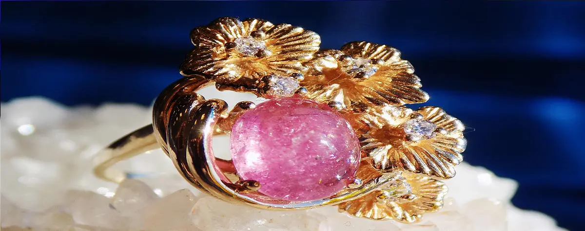 A pink stone is sitting on some gold flowers